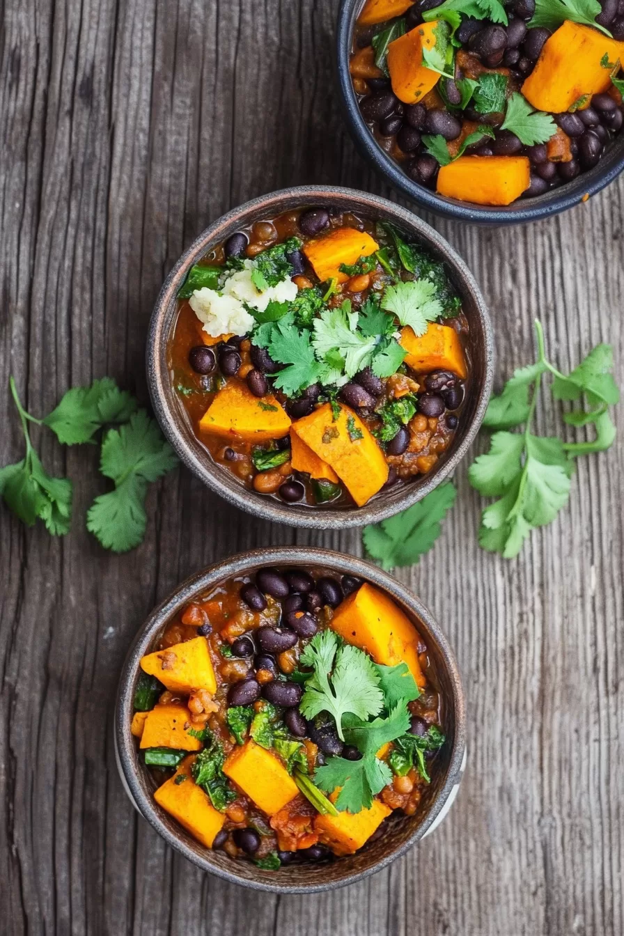 Top view of three bowls filled with a rich and flavorful sweet potato and black bean stew, surrounded by fresh cilantro leaves.