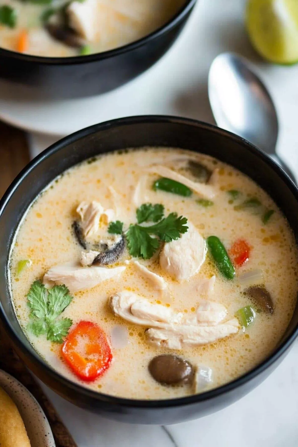 Close-up of a steaming bowl of soup featuring vibrant red chili slices and a sprinkle of cilantro.