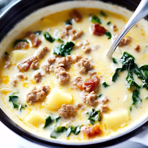 A ladle lifting a creamy soup loaded with savory sausage and tender potatoes from a pot.