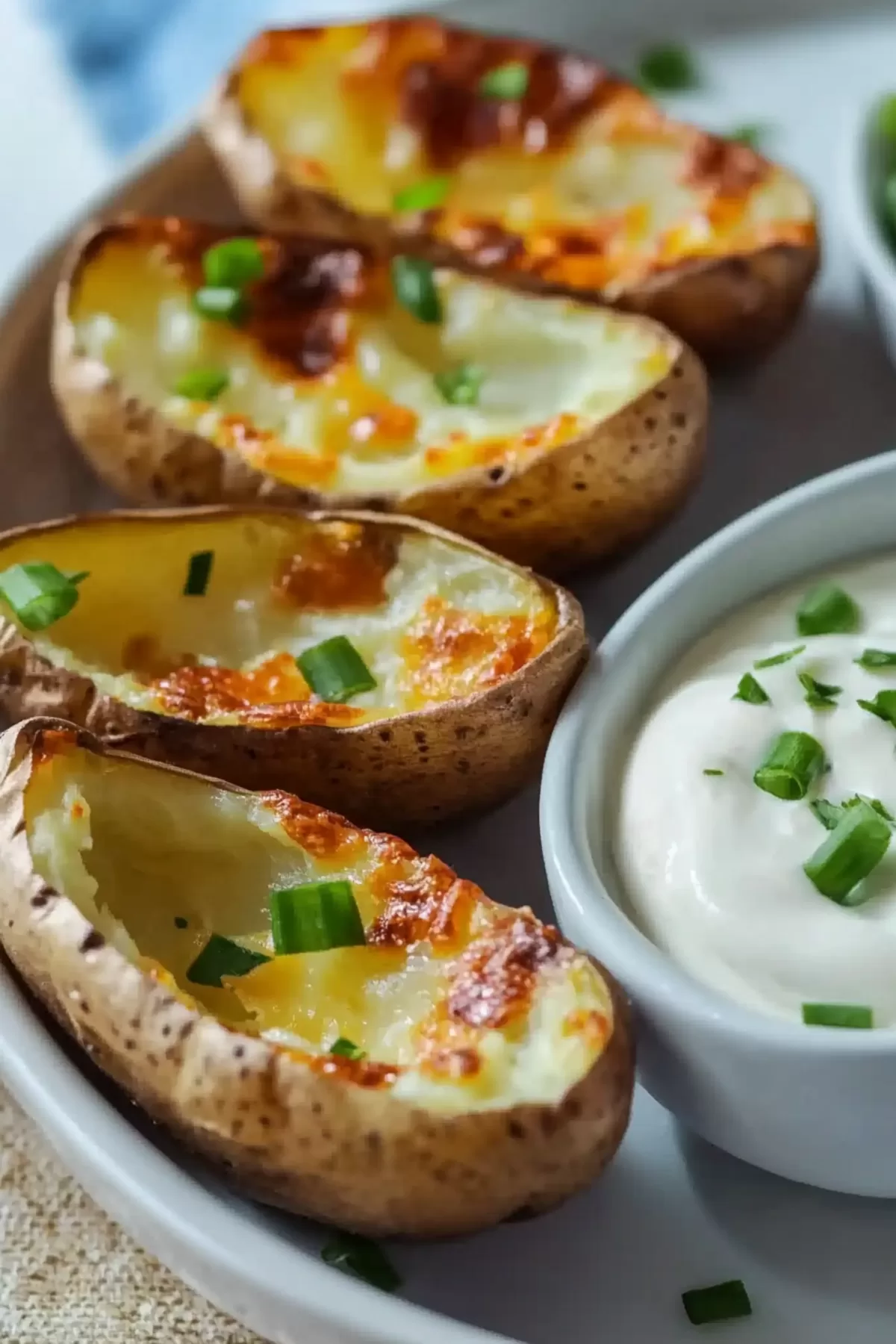 Baked potato skins fresh from the oven, served with a side of creamy dipping sauce and sprinkled with scallions.