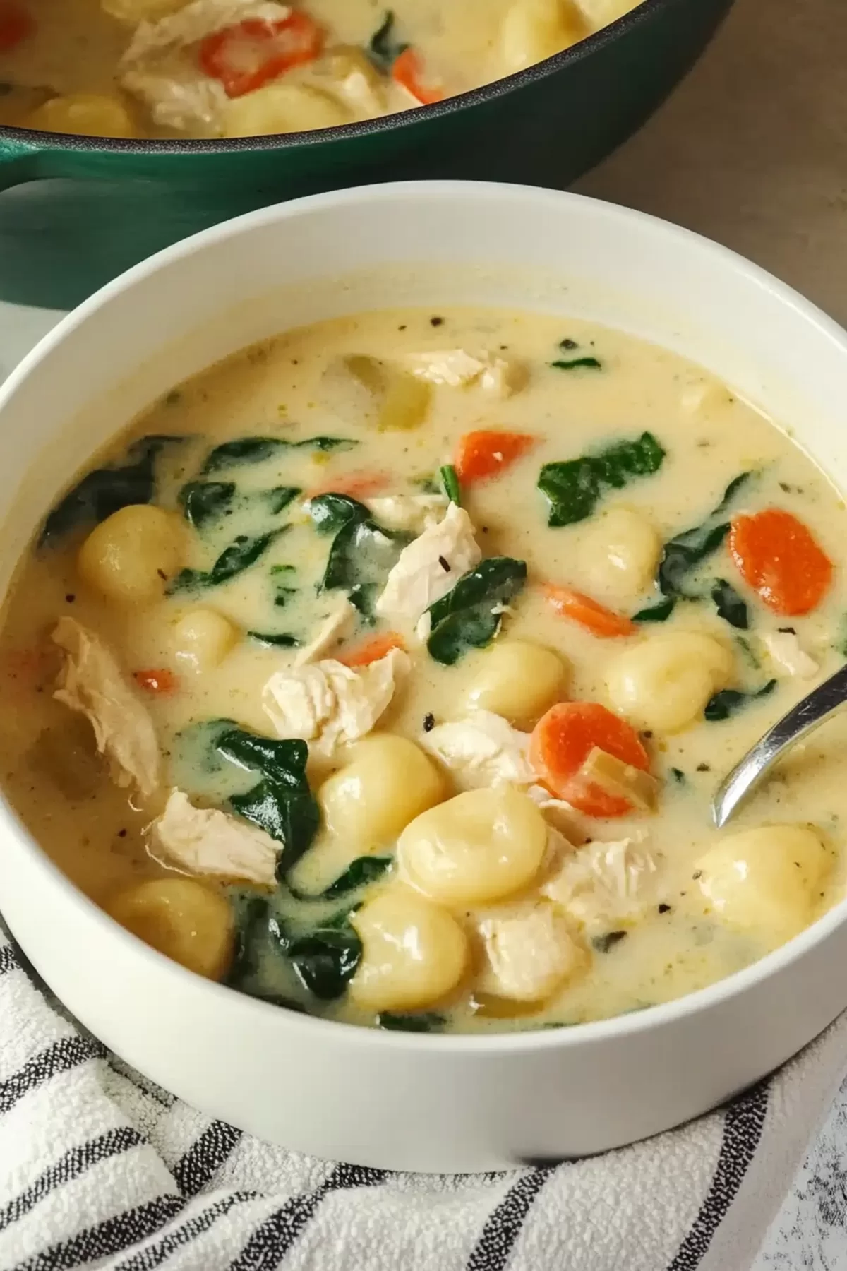 A steaming pot of chicken gnocchi soup garnished with freshly cracked black pepper, ready to serve.