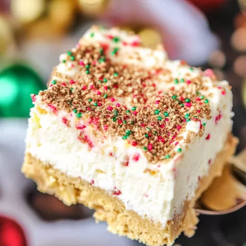 A thick dessert square with a golden cookie crust and whipped cream layer, sprinkled with colorful holiday decorations.