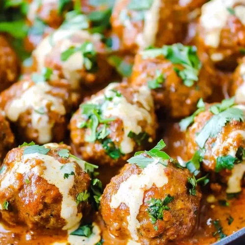 Close-up of tender meatballs coated in a vibrant coconut curry sauce with a drizzle of cream.