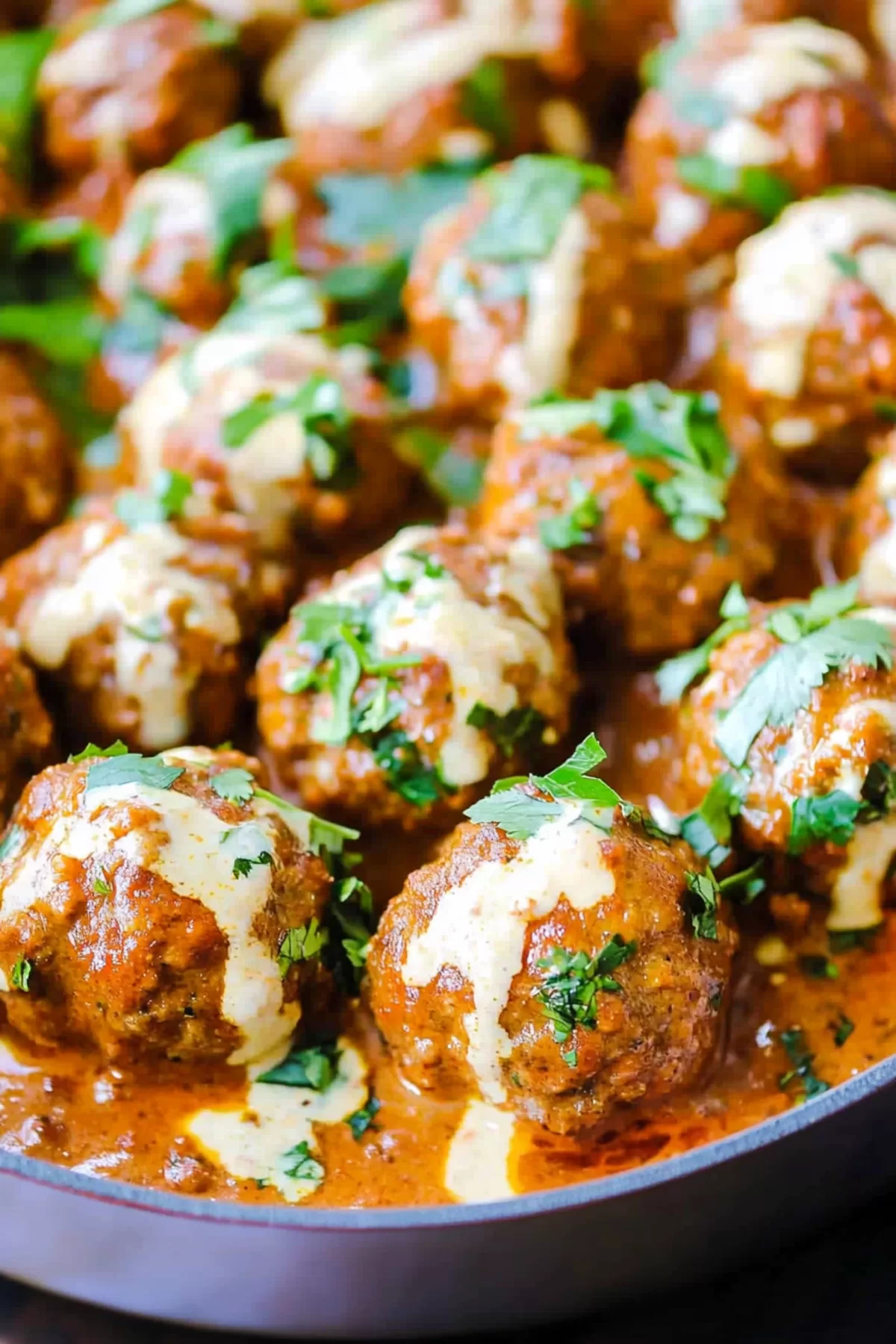 Close-up of tender meatballs coated in a vibrant coconut curry sauce with a drizzle of cream.