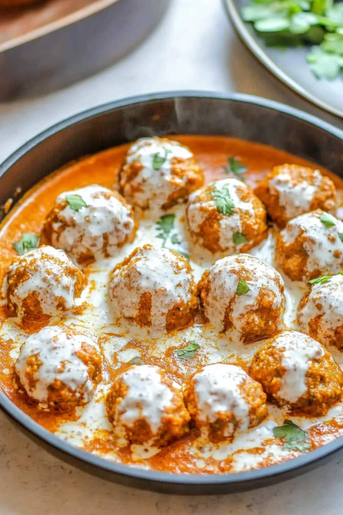 Coconut curry meatballs glistening in a creamy sauce, topped with fresh cilantro and spices.