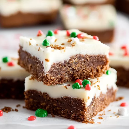 Close-up of layered gingerbread cookie bars with a rich icing layer, sprinkled with red and green decorations.