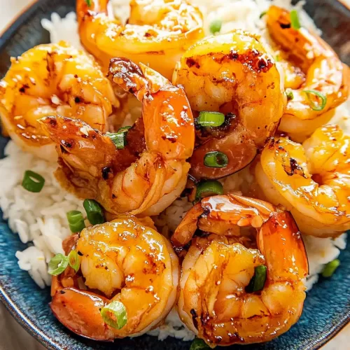 A bowl of honey garlic shrimp served over fluffy white rice with a wedge of lime on the side.