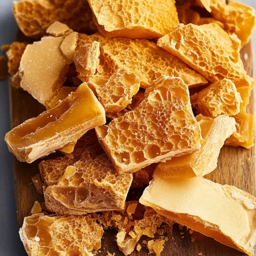 An arrangement of honeycomb candy pieces on a wooden board, displaying their intricate texture and glossy surface.