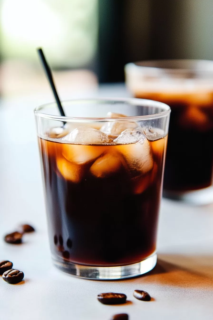 Two glasses of cold brew coffee with ice cubes, sitting on a marble countertop.