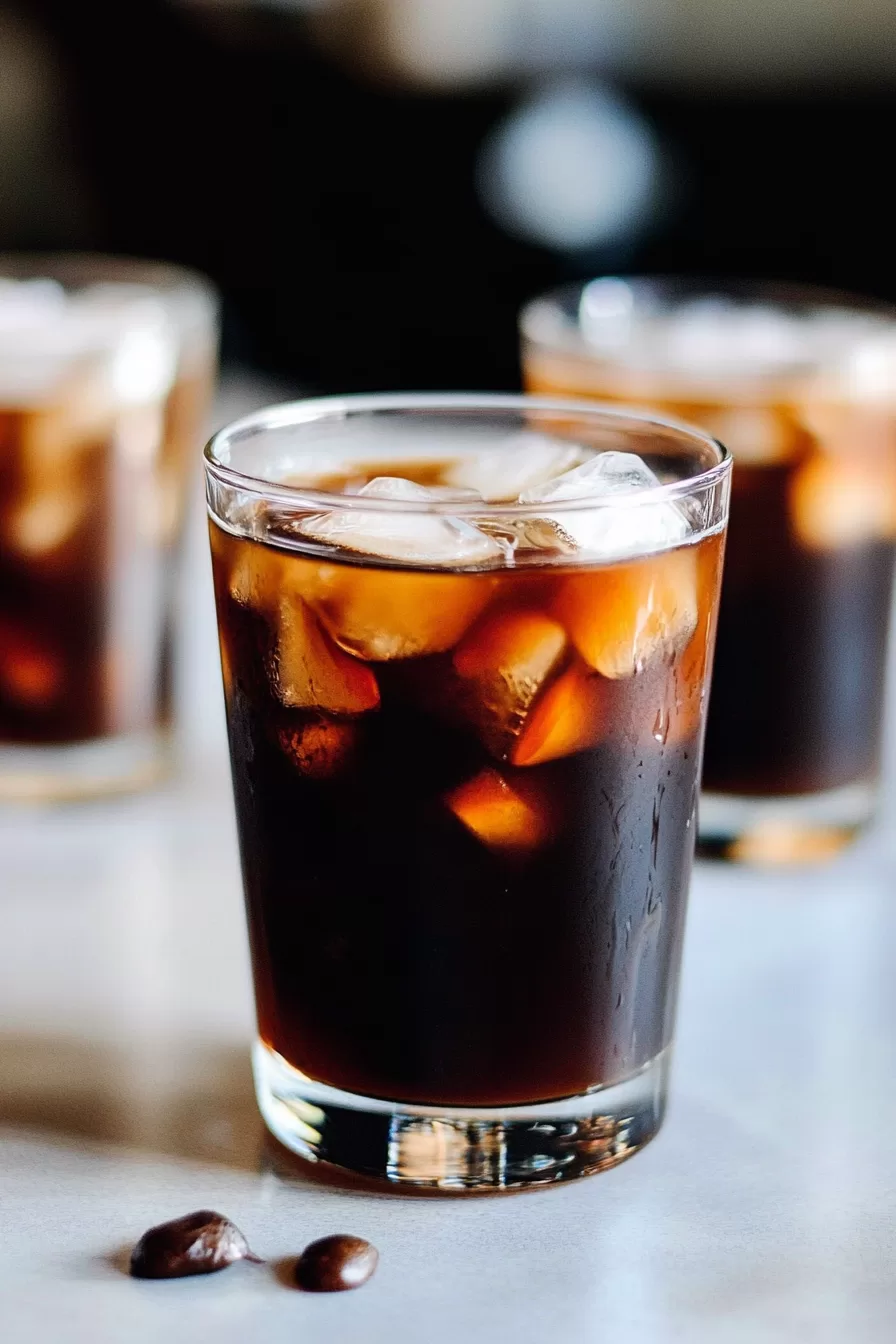 Multiple glasses of iced coffee with visible coffee beans scattered on the surface.