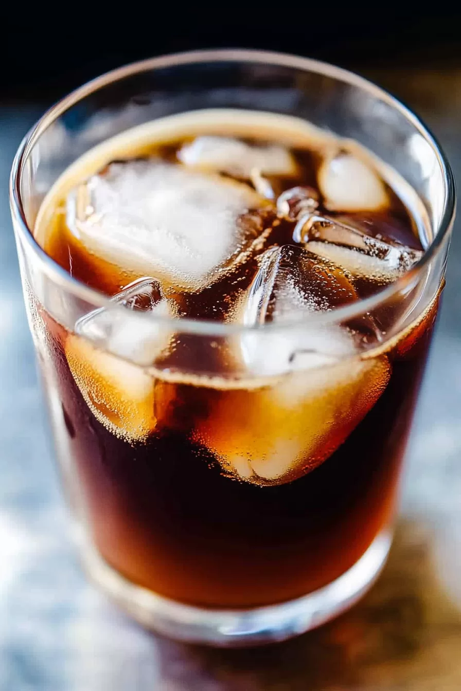 Close-up of a refreshing iced coffee in a glass with ice cubes and a straw on a bright table.