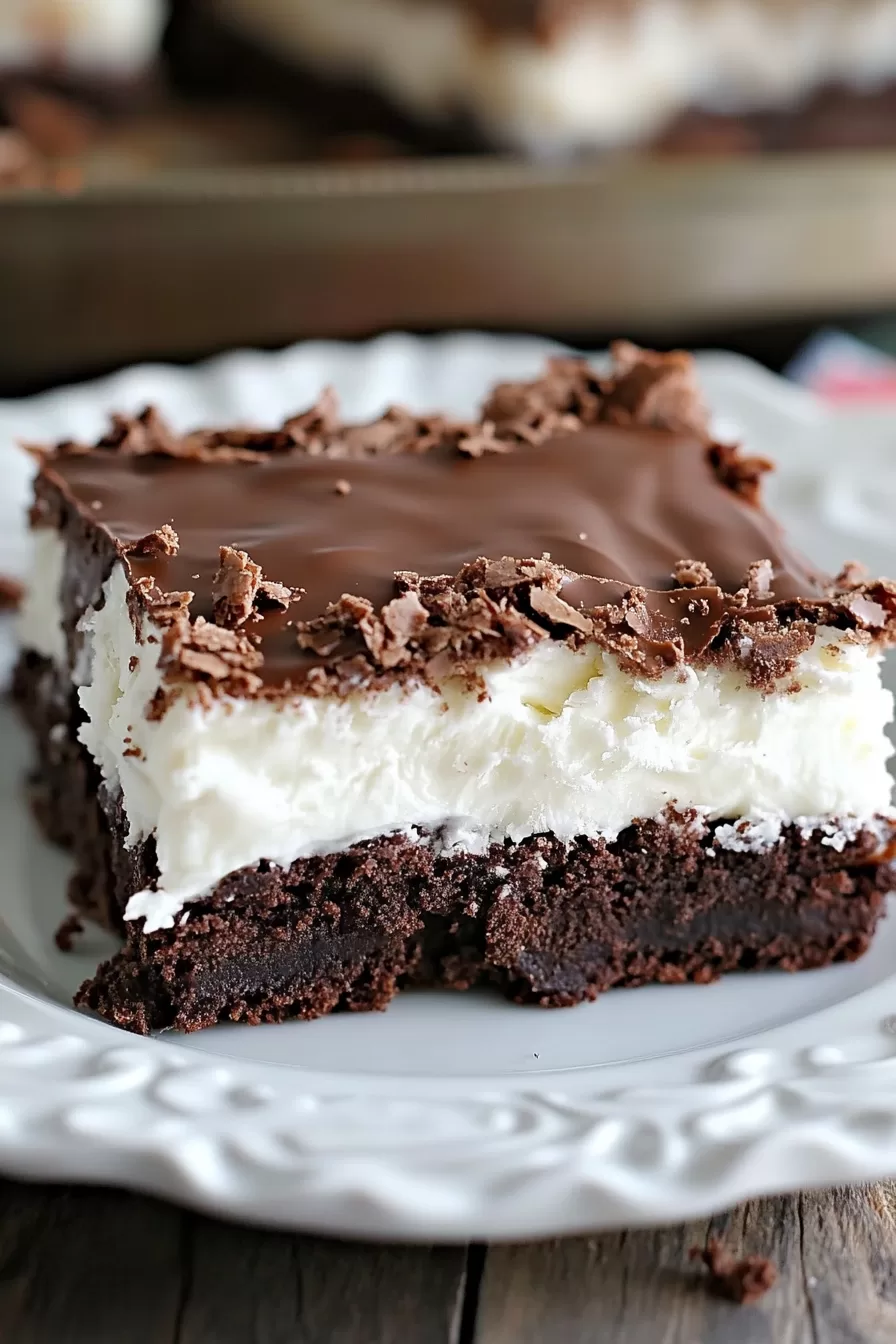 A rich brownie topped with creamy coconut filling and a glossy chocolate layer on a white plate.