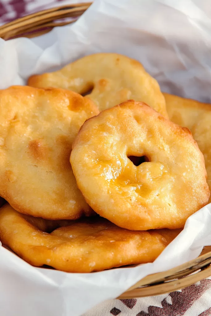 A close-up of crispy fry bread dusted with powdered sugar, resting on parchment paper.