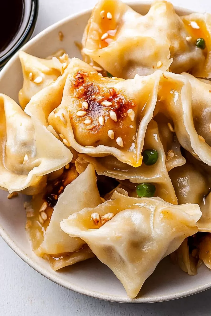 Close-up of golden pork wontons garnished with sesame seeds and served in a light soy dipping sauce.