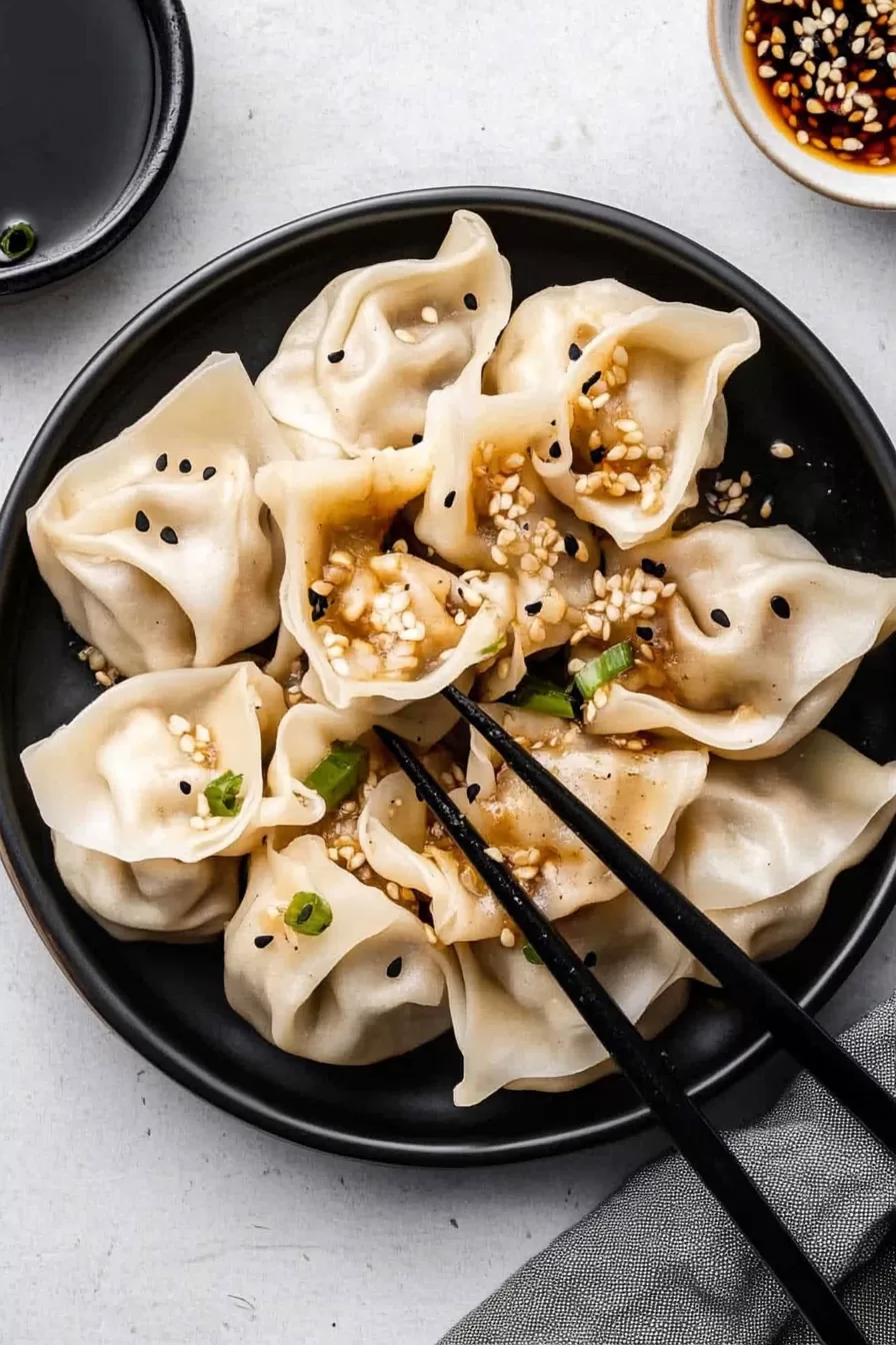 A black bowl filled with pork wontons, paired with a savory soy sauce for dipping.