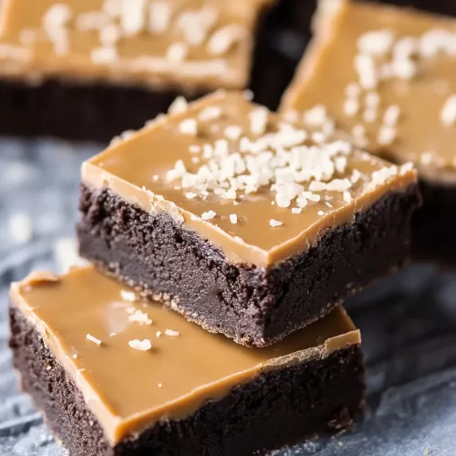 Close-up of a decadent chocolate sugar cookie bar layered with salted caramel and topped with a sprinkle of flaky salt.