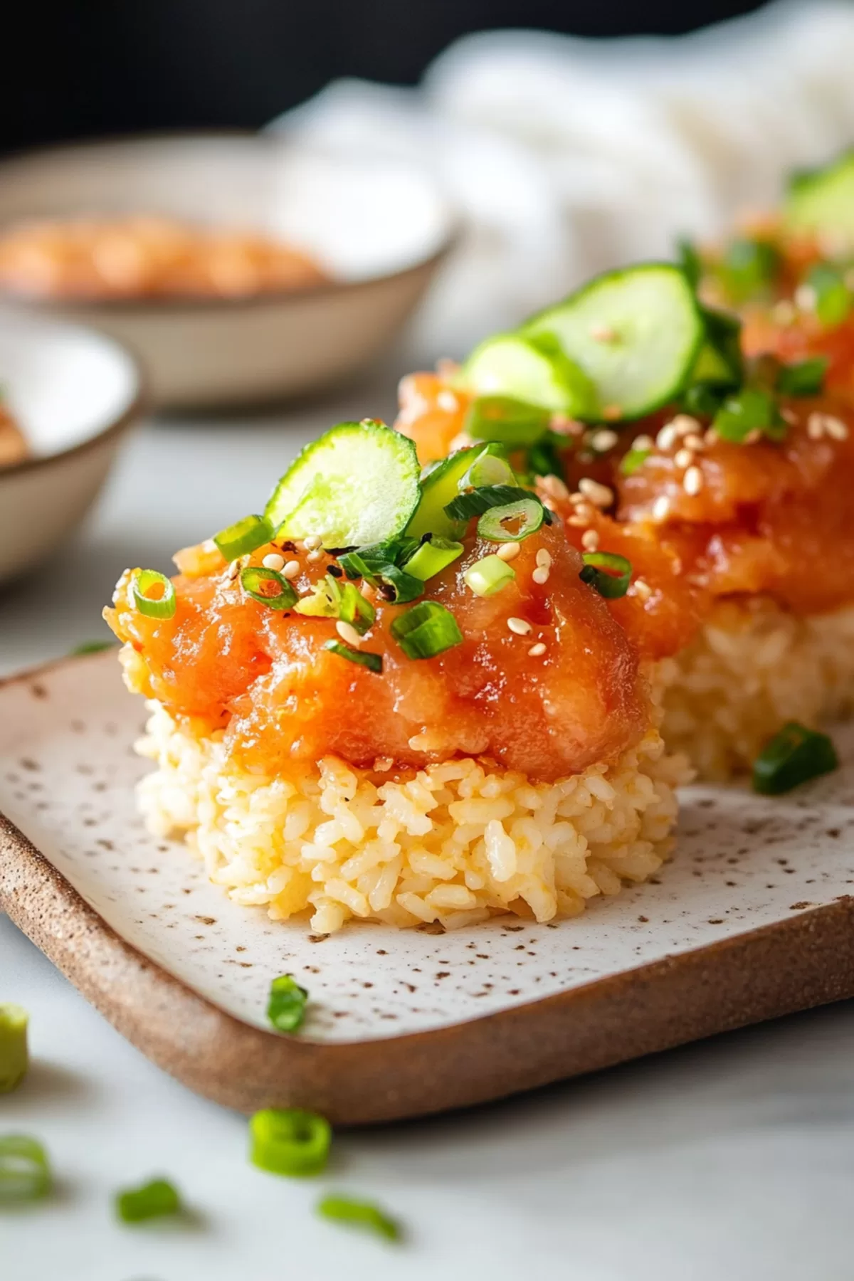 Close-up of crispy rice topped with spicy tuna and fresh cucumber slices, garnished with green onions and sesame seeds.