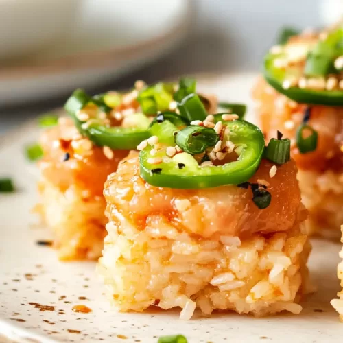 A plate featuring spicy tuna crispy rice bites, layered with jalapeño slices and sprinkled with sesame seeds.