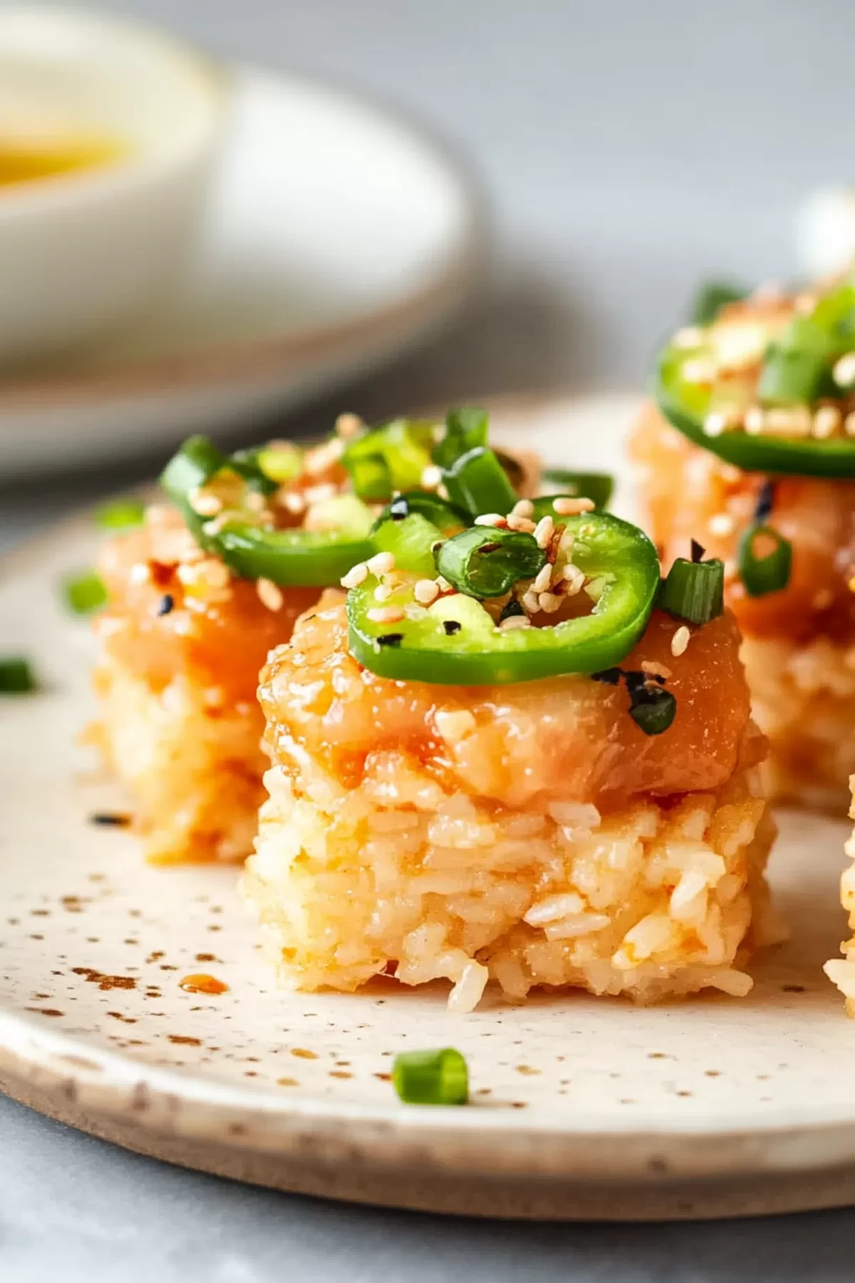 A plate featuring spicy tuna crispy rice bites, layered with jalapeño slices and sprinkled with sesame seeds.