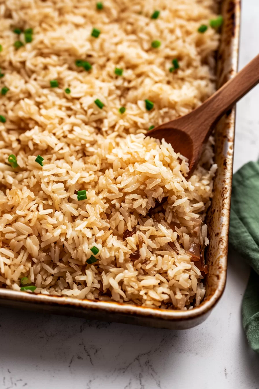 Serving spoon lifting perfectly cooked rice from a casserole dish, garnished with green onions.