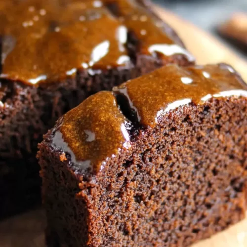 A slice of sticky ginger cake showcasing its rich texture and glossy glaze, perfect for a cozy dessert.