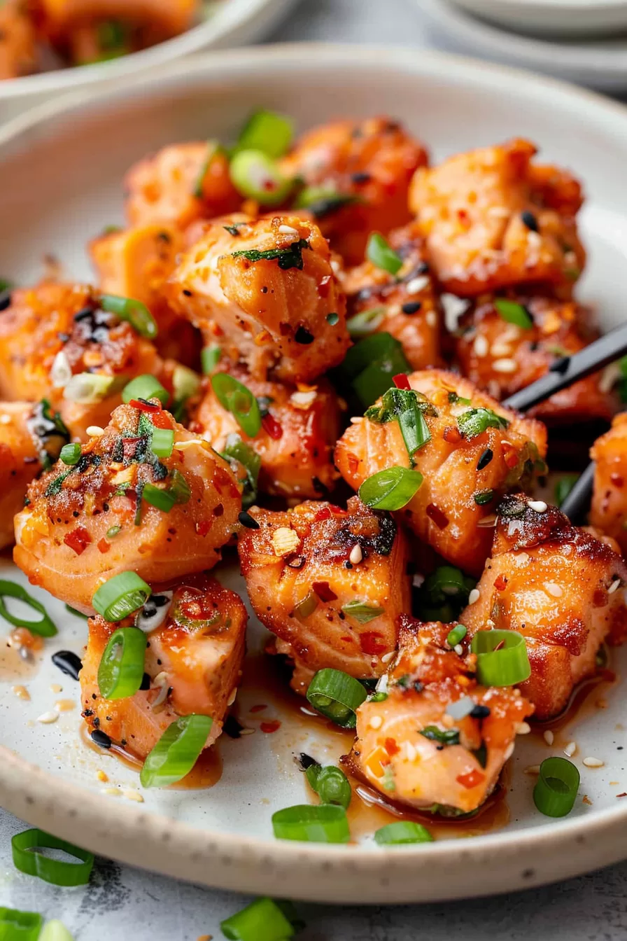 Close-up of crispy salmon bites garnished with chopped green onions and sesame seeds, drizzled with a spicy sauce.