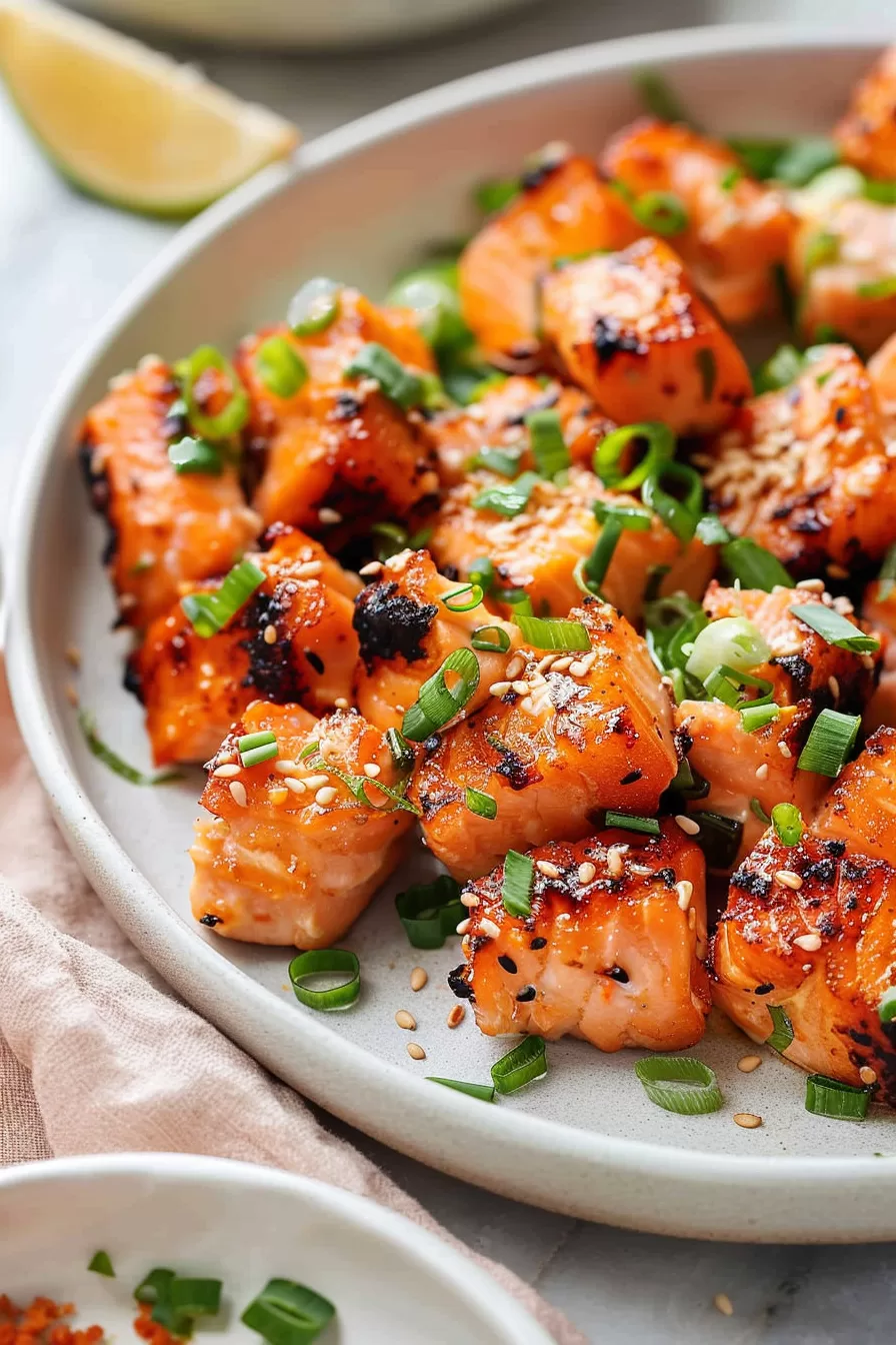 Perfectly seared salmon cubes with a caramelized glaze, topped with sesame seeds and fresh herbs on a white plate.