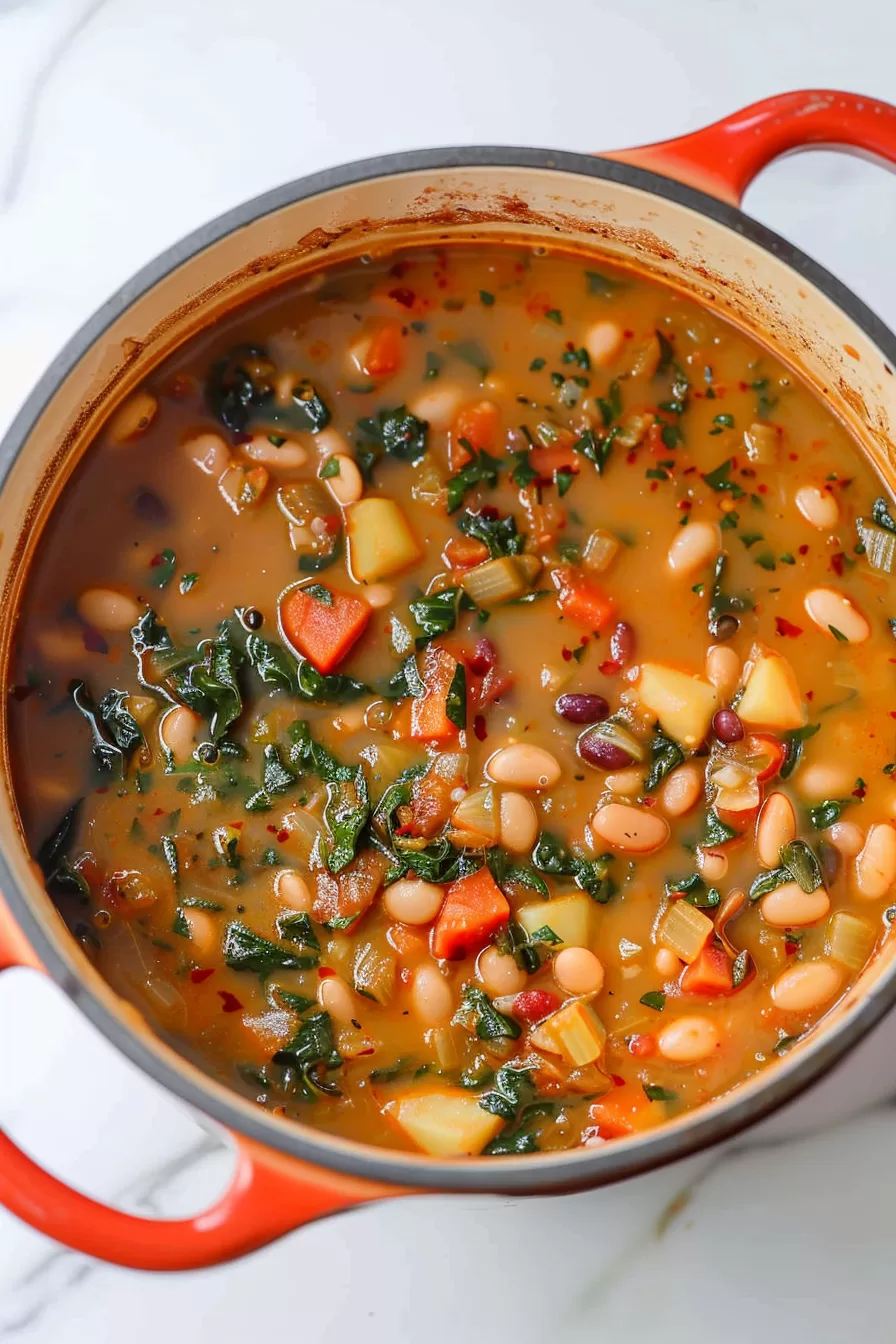 A top view of a cozy butter bean stew in a ceramic bowl, showing vibrant colors of beans, carrots, and leafy greens.