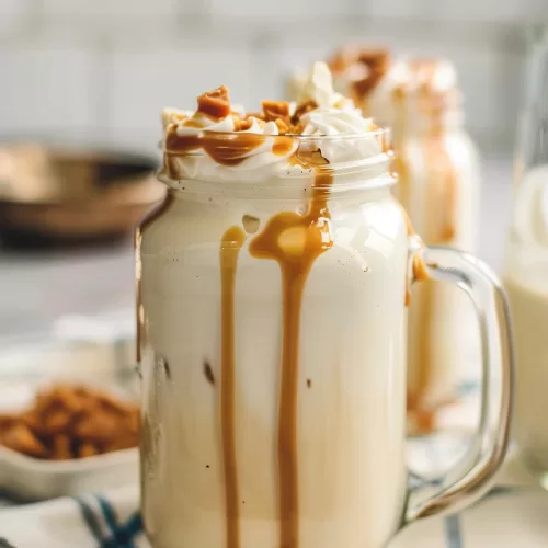 Glass jar filled with a smooth butterscotch shake, finished with whipped cream and caramel sauce running down the sides.