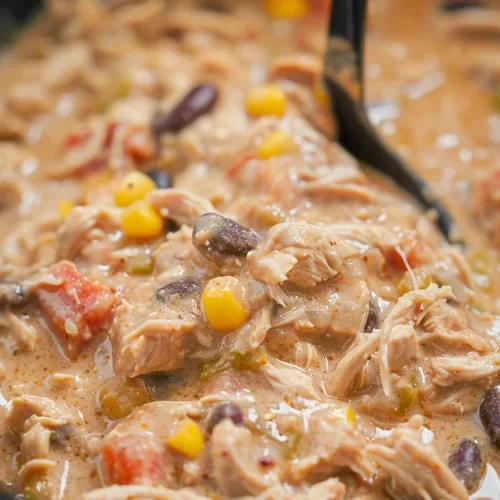 Rich and creamy chicken chili simmering in a slow cooker, showcasing its thick, comforting texture.