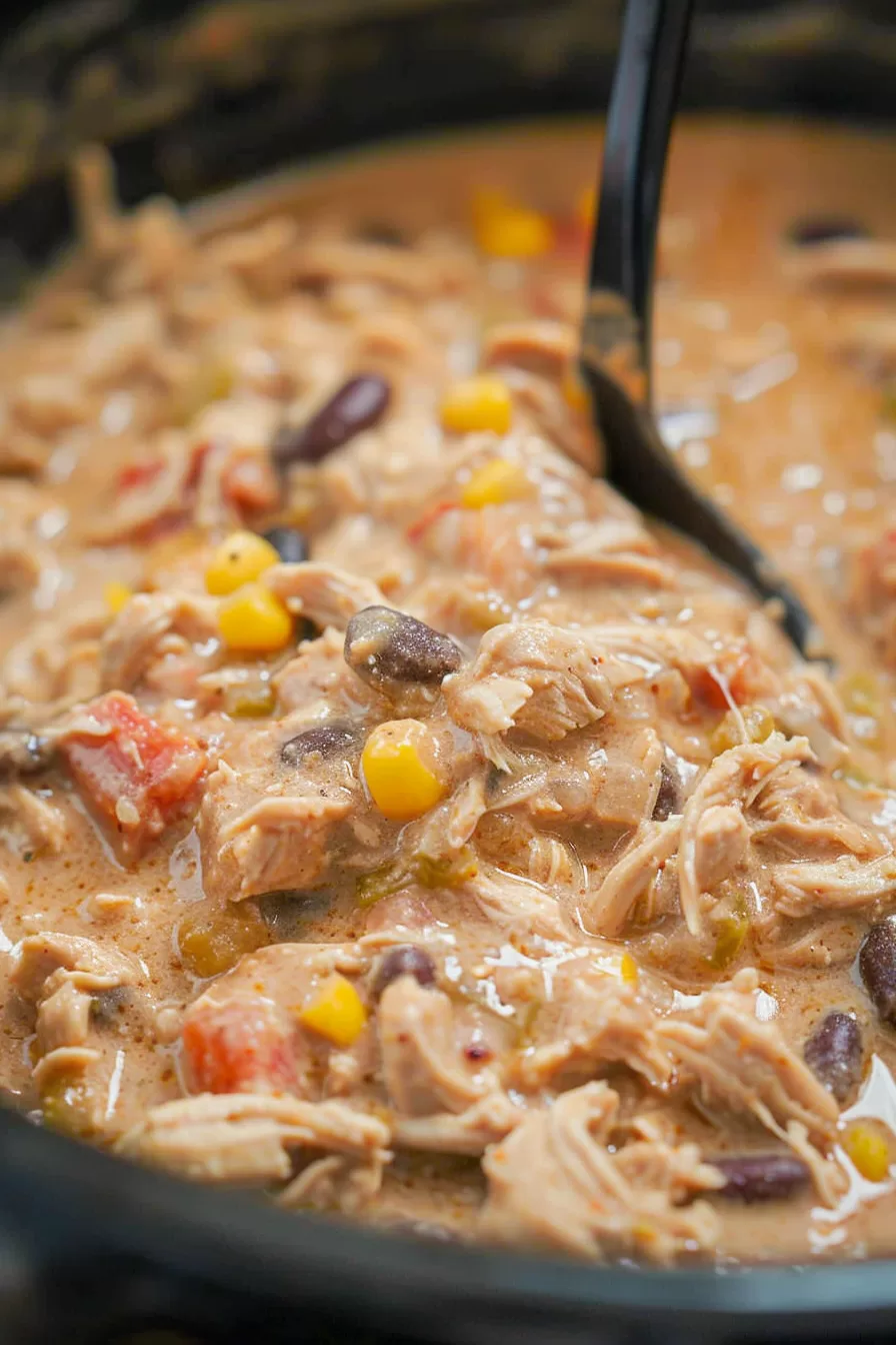 Rich and creamy chicken chili simmering in a slow cooker, showcasing its thick, comforting texture.