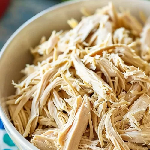 Close-up of tender shredded chicken breast served in a white bowl, perfect for meal prep or adding to various dishes.