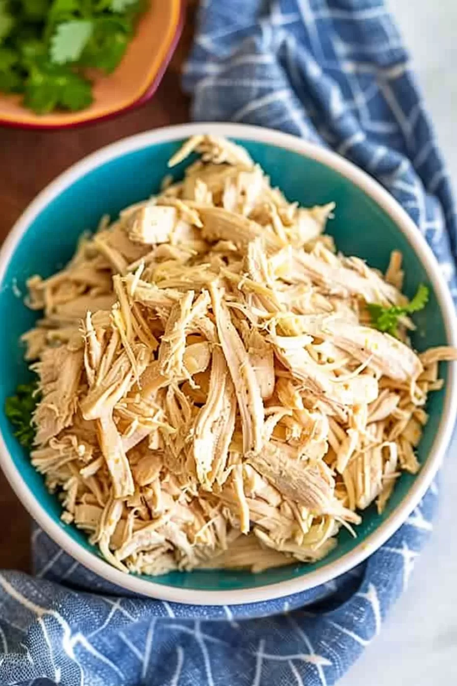 A bowl filled with freshly shredded chicken breast, cooked until tender and easily pulled apart for versatile recipes.