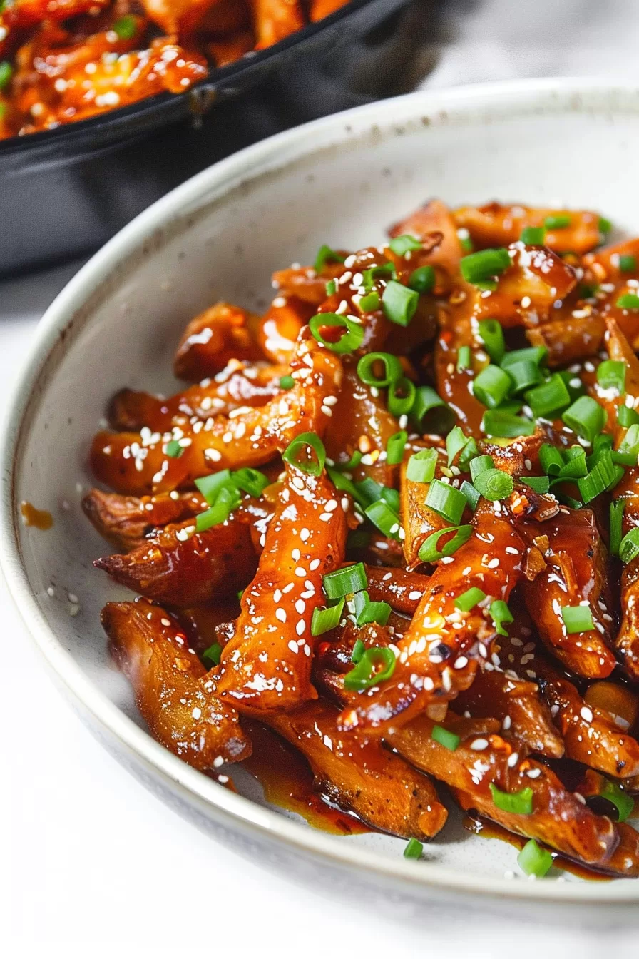 Honey chilli potato fries tossed in a rich, spicy sauce, finished with sesame seeds and vibrant green onions in a ceramic bowl.