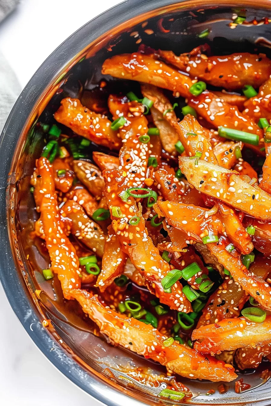 A bowl filled with sticky honey chilli potatoes, perfectly coated in a spicy-sweet glaze, topped with fresh herbs.