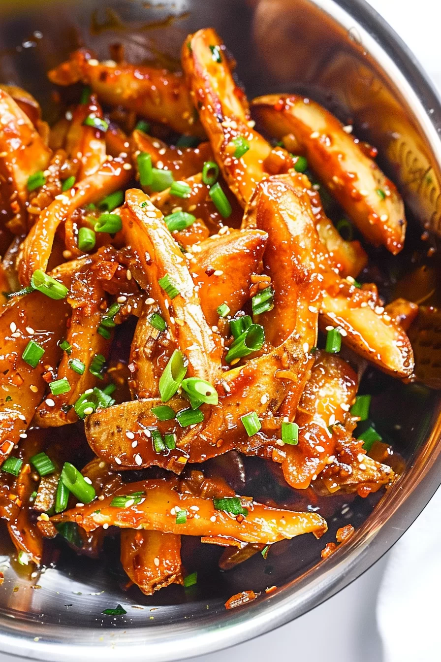 Skillet filled with crispy fried potatoes coated in a glossy honey chilli sauce, with sesame seeds and sliced green onions for garnish.