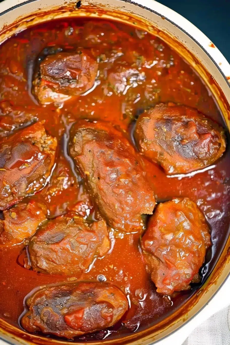 Close-up of tender meatballs simmering in a rich tomato sauce in a blue enameled Dutch oven.