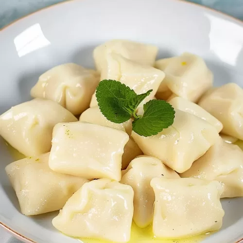 A plate of homemade dumplings dusted with powdered sugar and topped with fresh mint leaves.