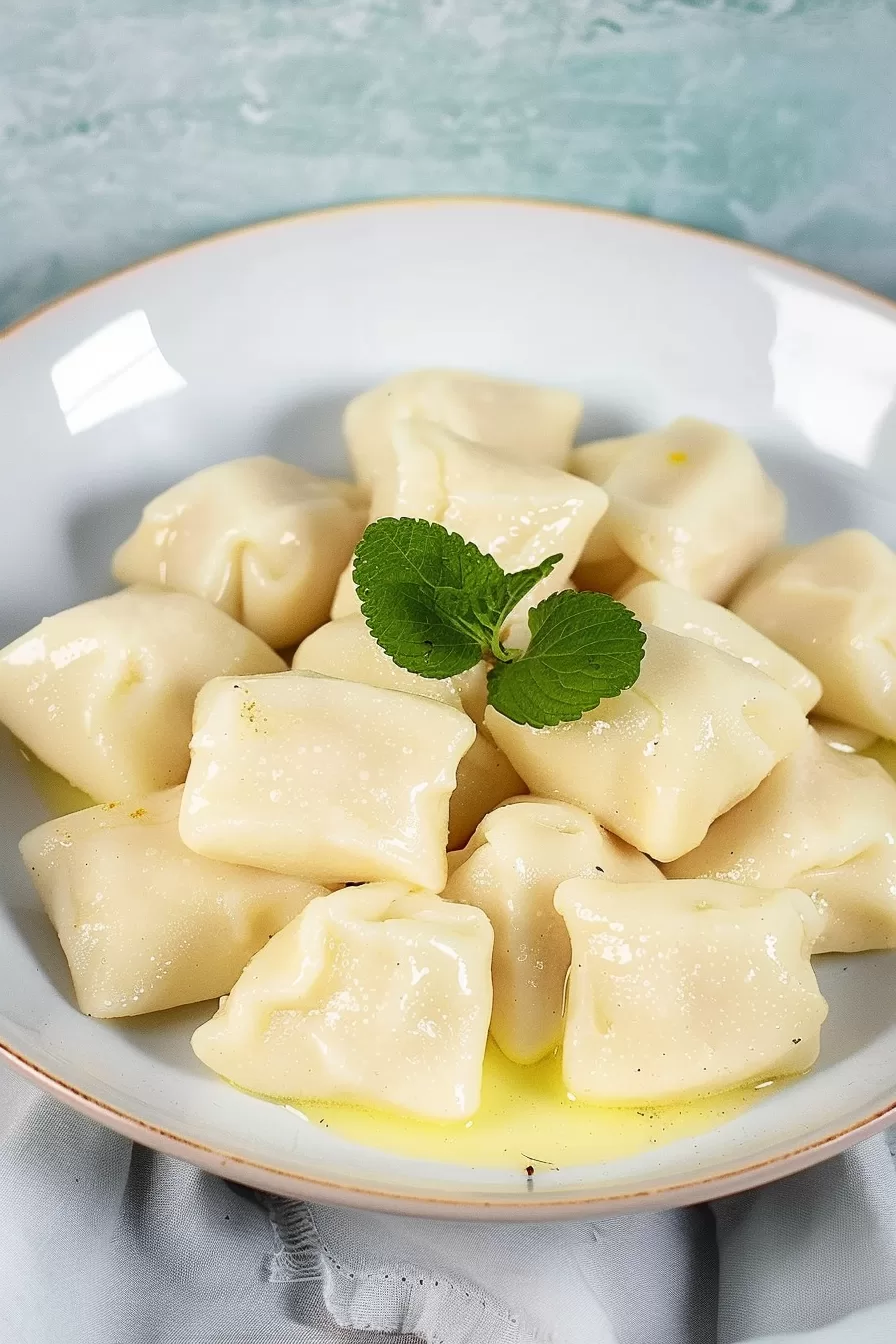 A plate of homemade dumplings dusted with powdered sugar and topped with fresh mint leaves.