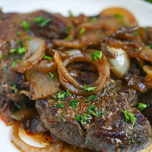 Close-up of a plate of liver and onions with rich brown gravy, garnished with finely chopped herbs.