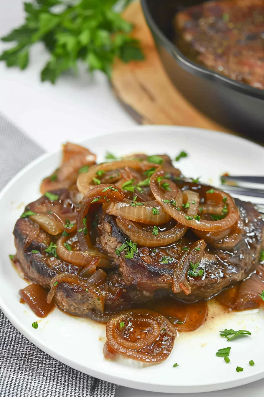 A hearty serving of liver and onions with a glossy sauce, presented on a white plate with a side of mashed potatoes.