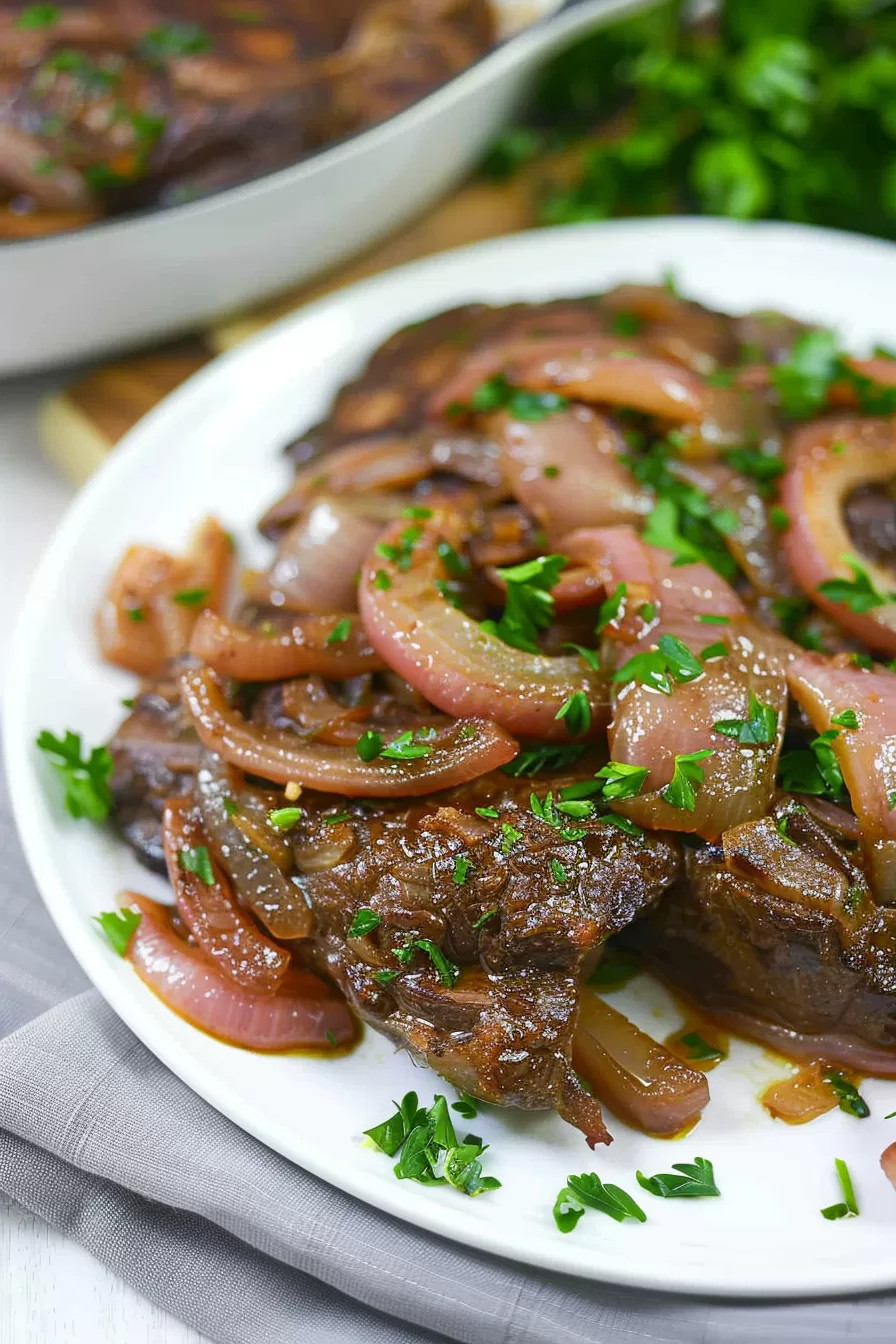 Seared liver topped with sweet, translucent onions and a sprinkle of parsley, ready to serve for a comforting dinner.