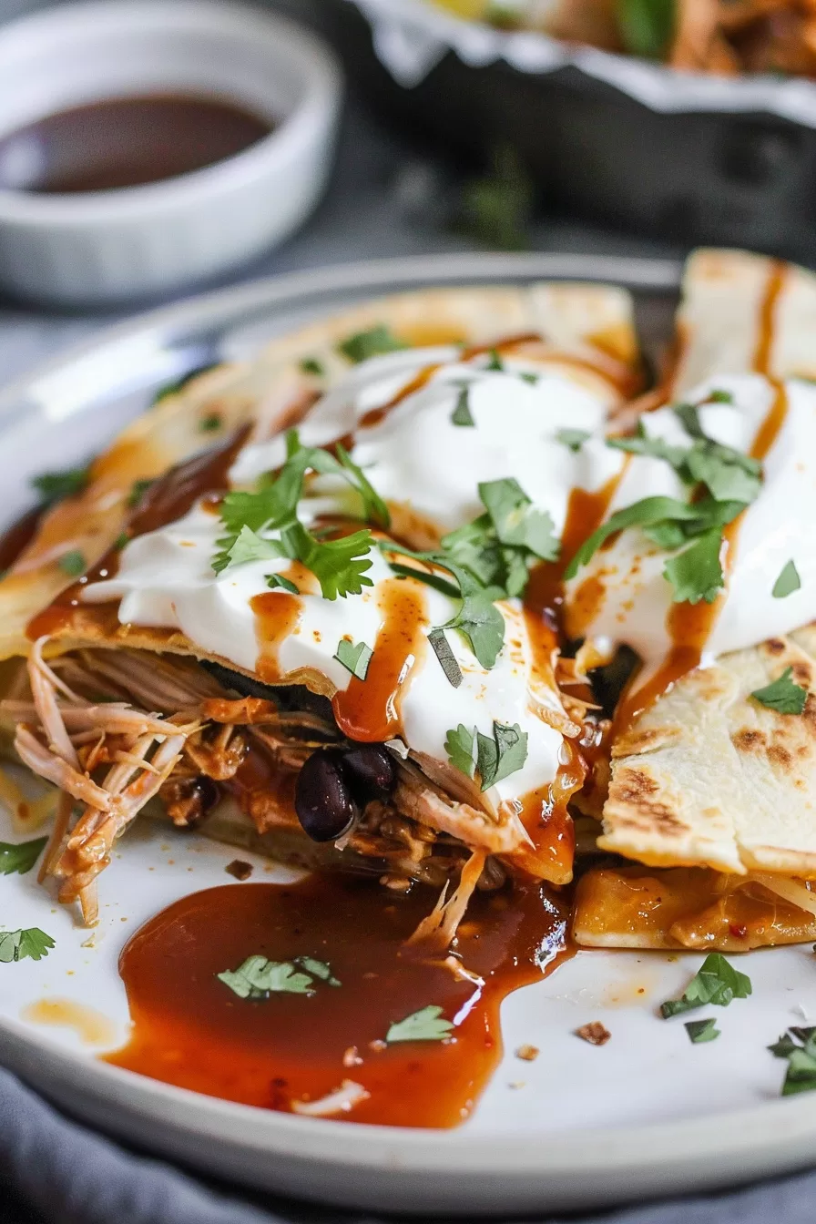 Crispy quesadilla wedges filled with tender pork carnitas and melted cheese, garnished with chopped cilantro and a drizzle of barbecue sauce.