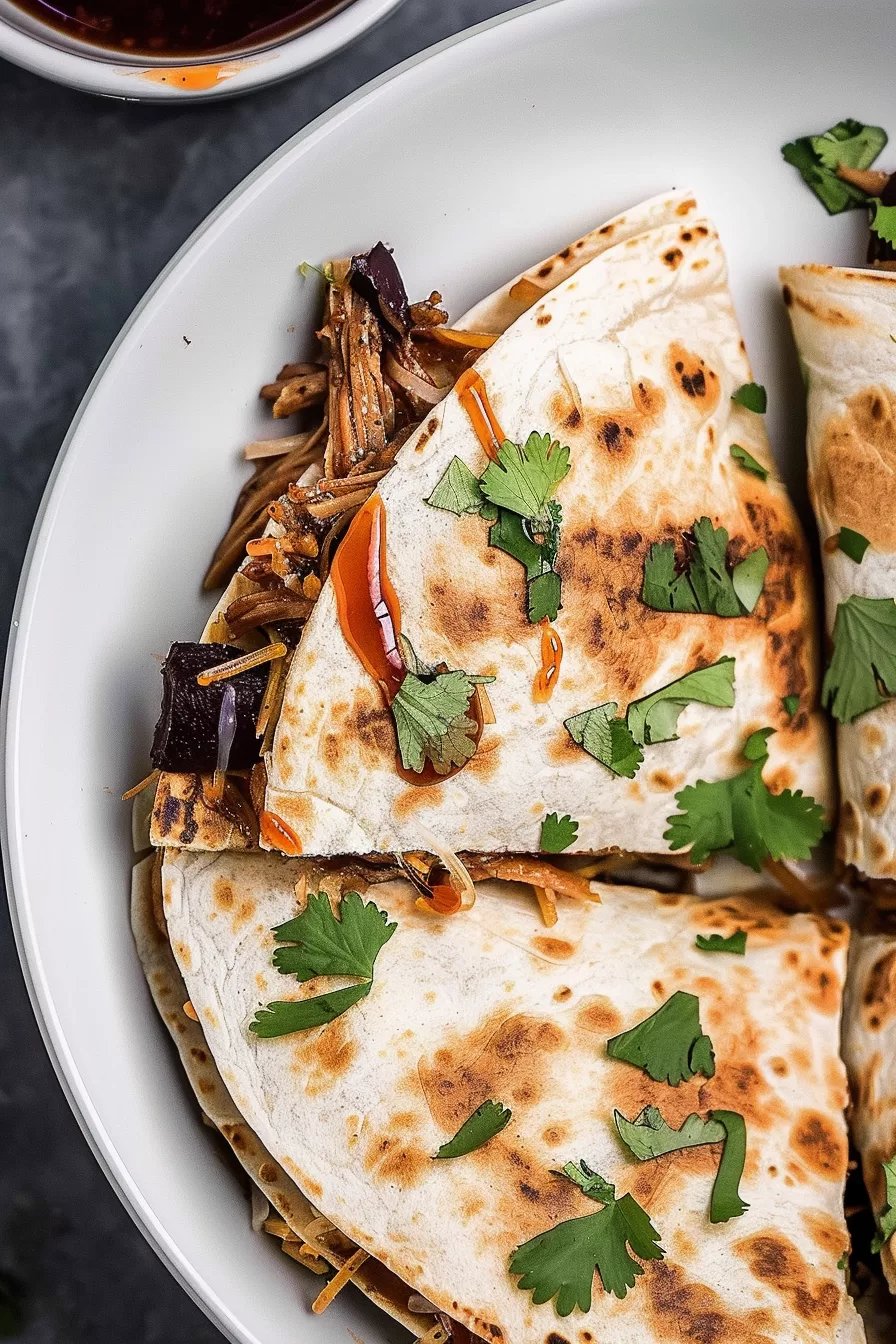 A plate of crispy pork carnitas quesadillas, loaded with shredded meat, melted cheese, and a touch of barbecue sauce for extra flavor.