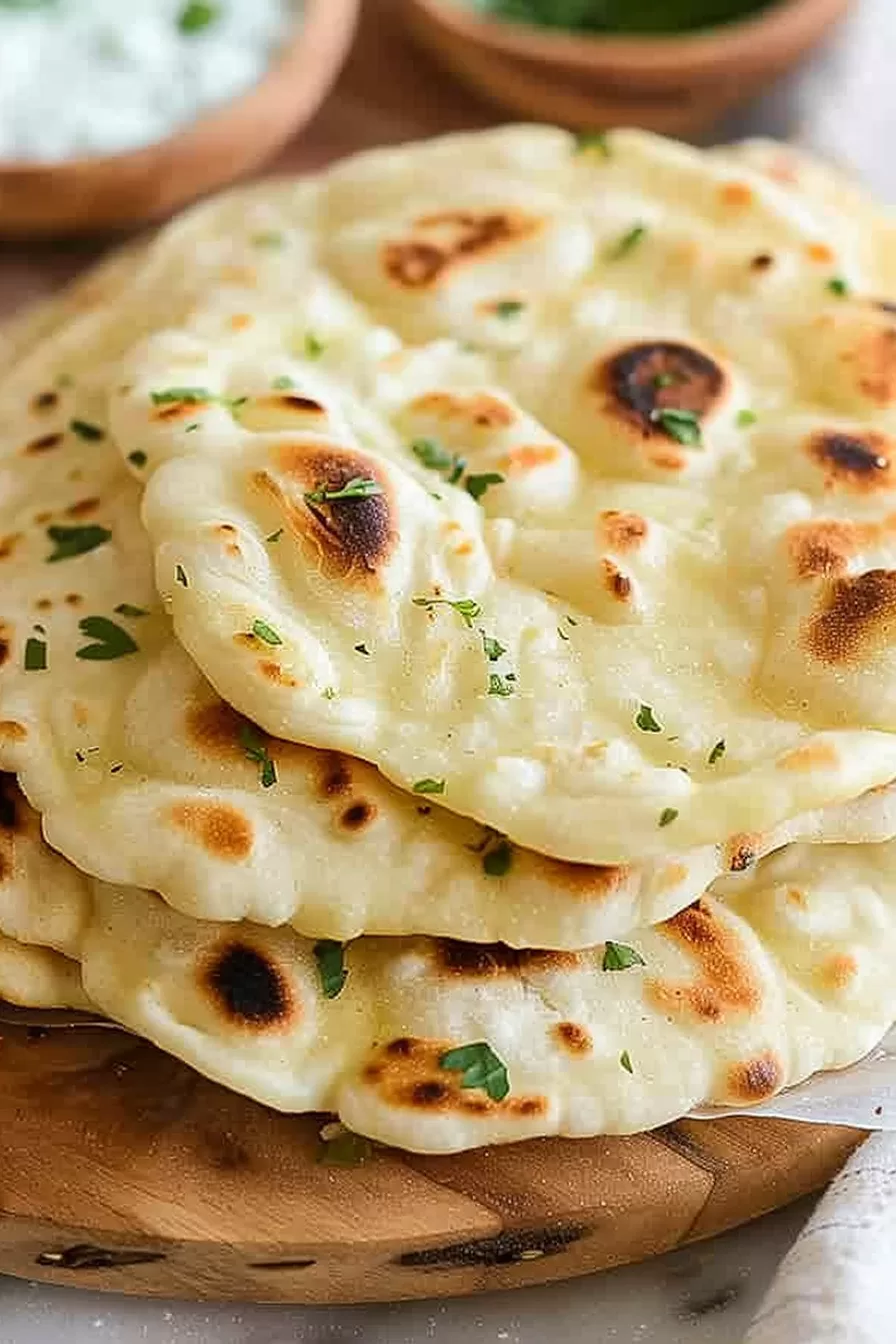 Close-up of freshly made roti bread with a golden, charred surface, brushed with butter and garnished with chopped herbs.