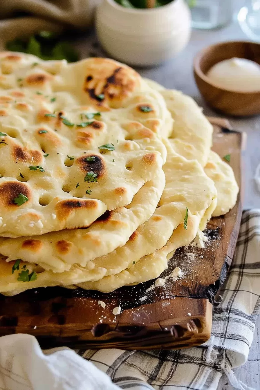 Pile of warm, buttery roti bread with visible grill marks, ready to be served alongside a bowl of curry.