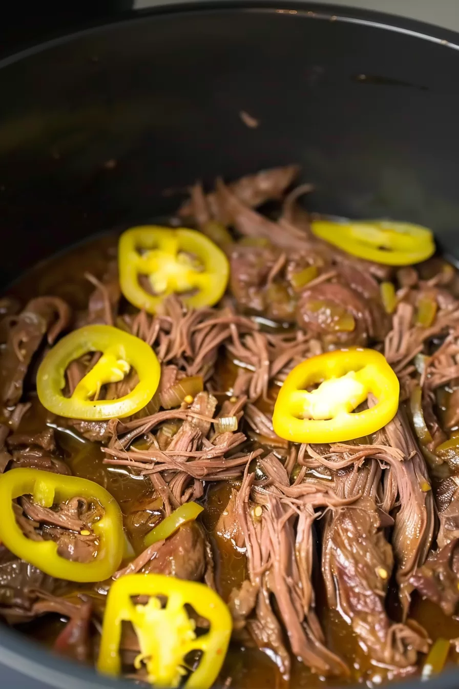 Close-up of juicy, slow-cooked beef roast with sliced yellow peppers and a savory gravy coating the meat.