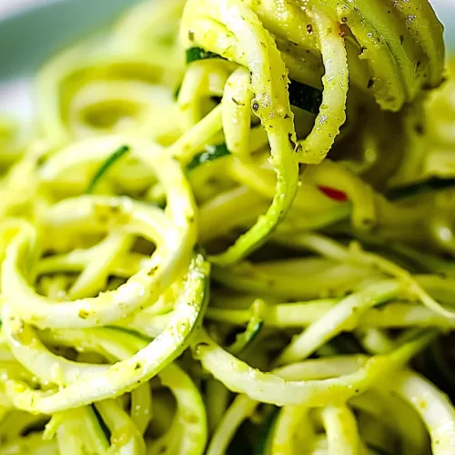 A bowl of zucchini noodles mixed with pesto, ready to serve, showcasing their glossy texture and seasoning.