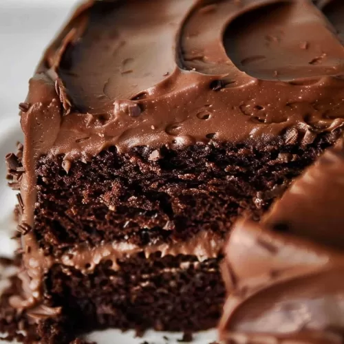 A partially sliced chocolate cake with chocolate frosting, highlighting the cake's moist texture and creamy layers.