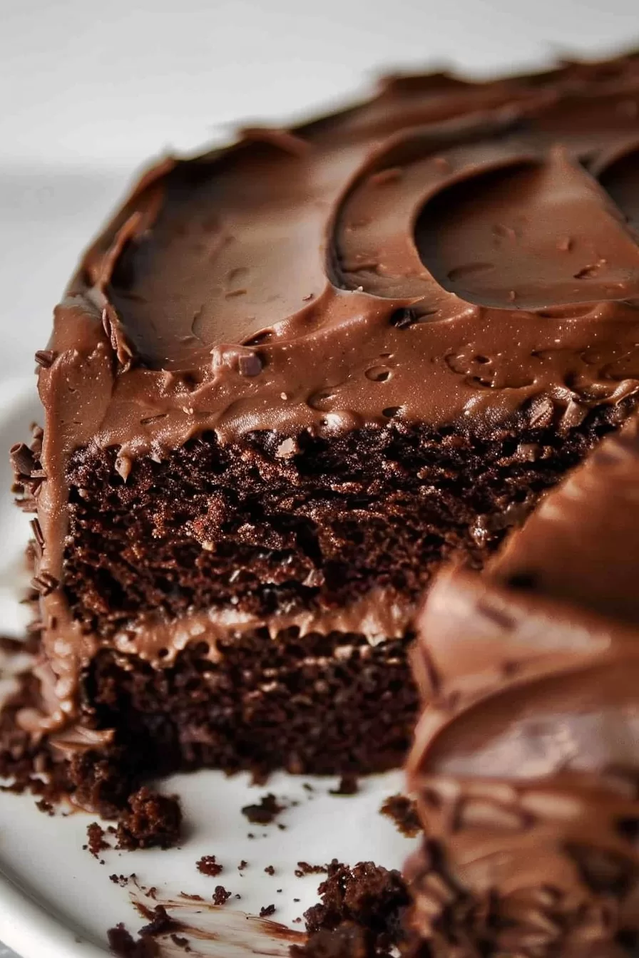 A partially sliced chocolate cake with chocolate frosting, highlighting the cake's moist texture and creamy layers.